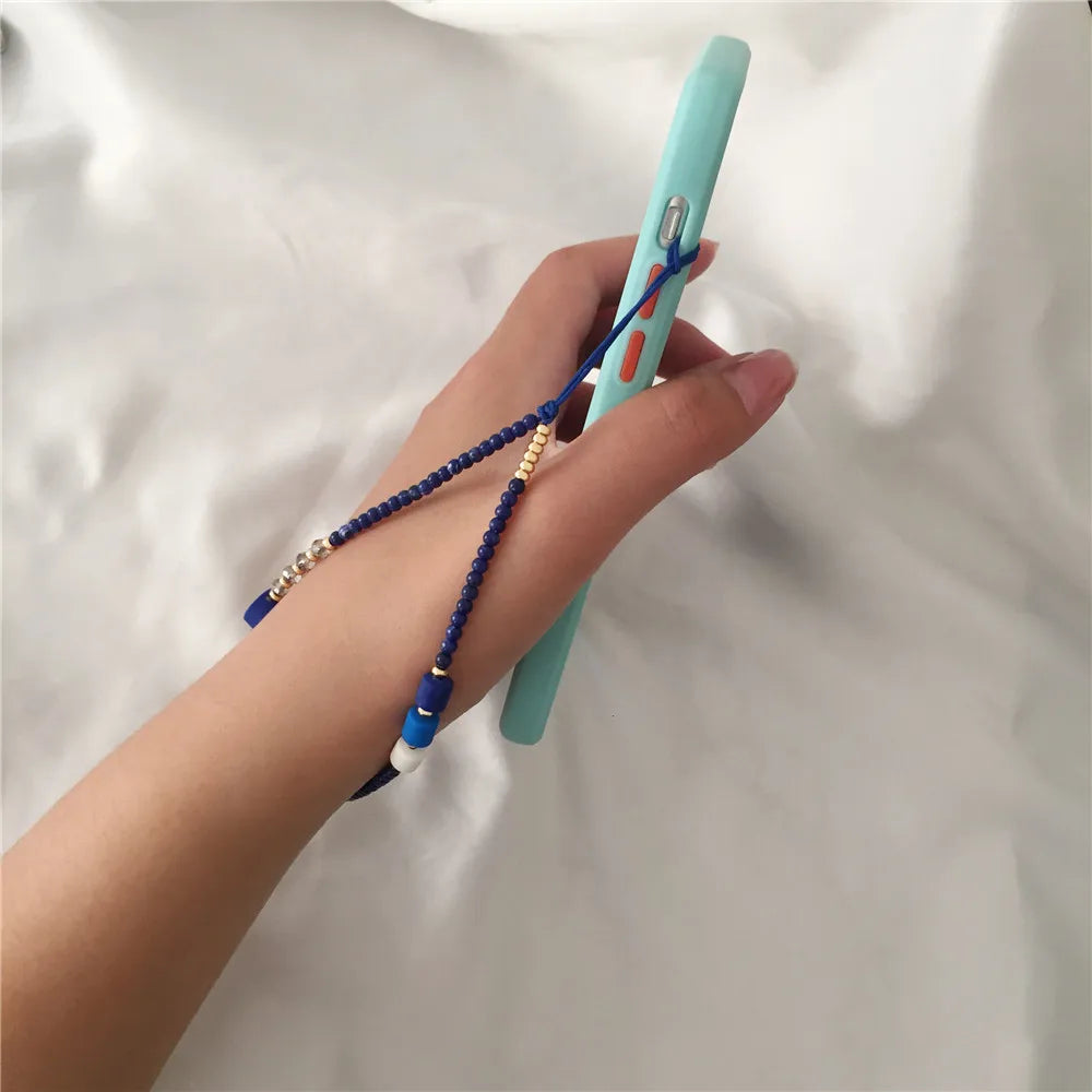 Hand holding a turquoise phone case with a blue beaded strap on a light background
