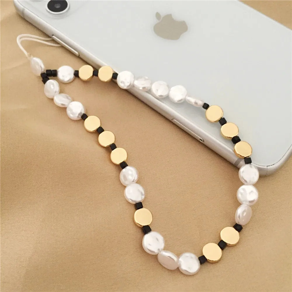 Phone lanyard with pearls and gold accents on a beige surface