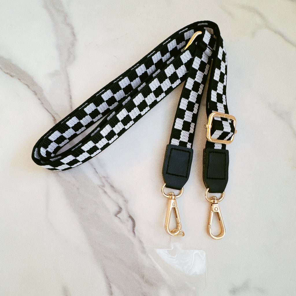 Black and white checkered phone crossbody with gold hardware on a marble surface