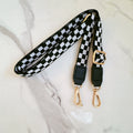 Black and white checkered phone crossbody with gold hardware on a marble surface