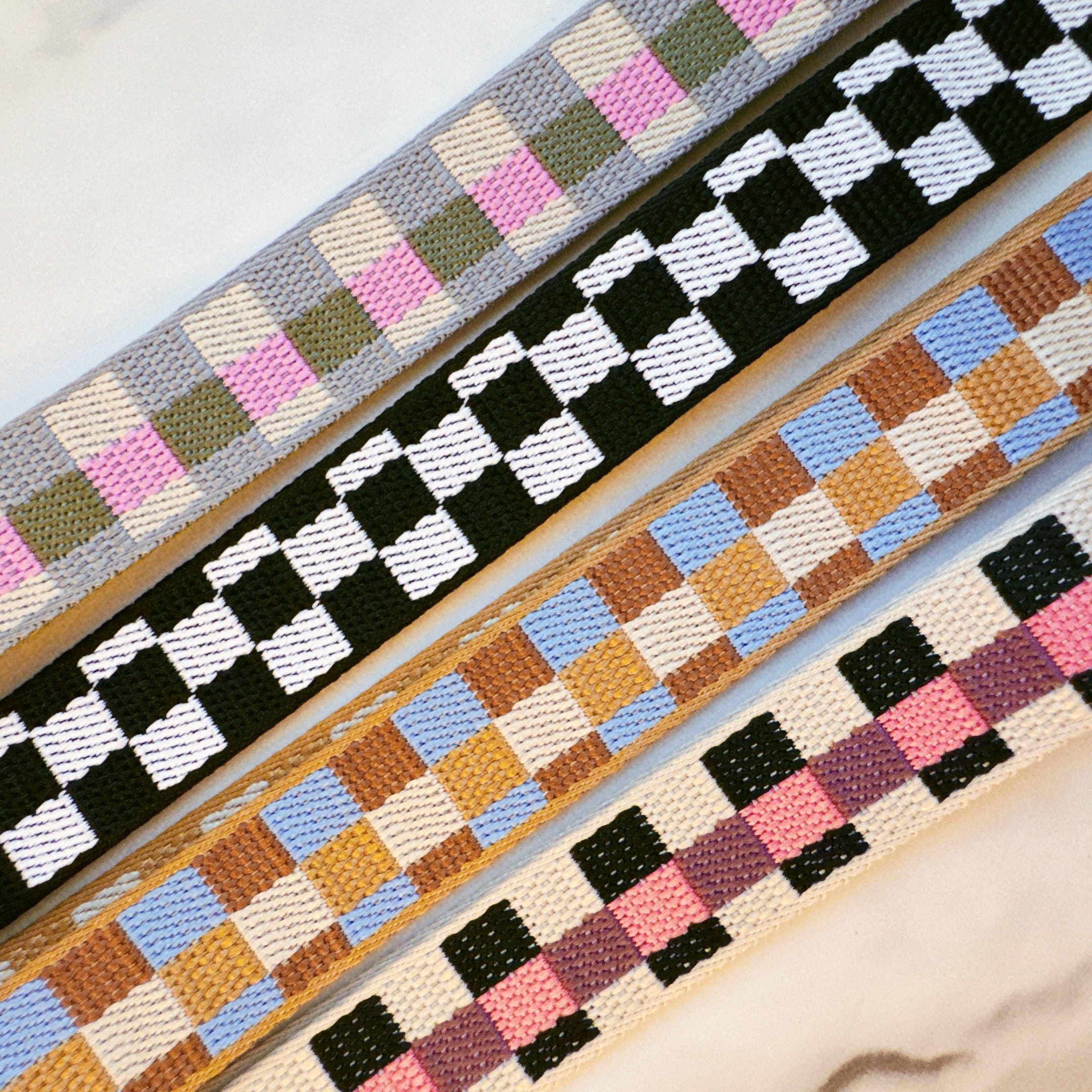 Four woven straps with different checkered patterns on a light background